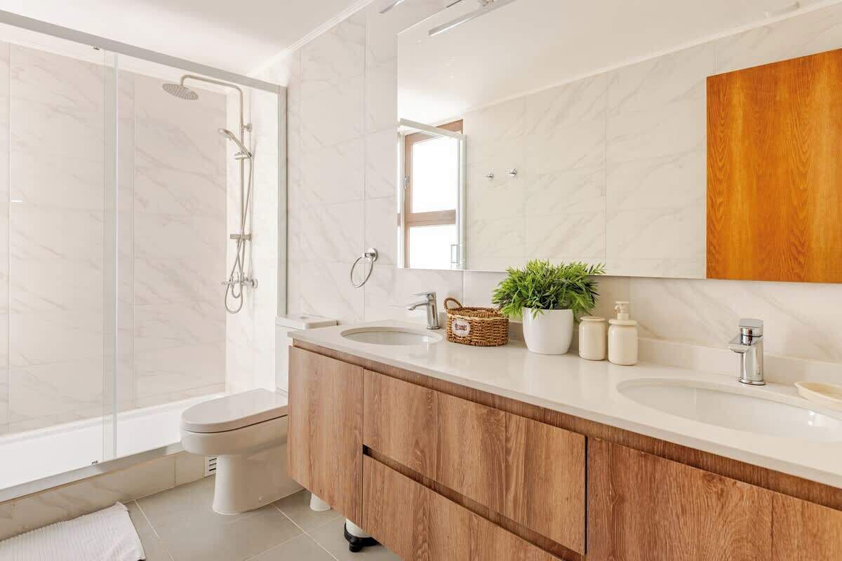 A modern bathroom with a glass shower enclosure, a wooden vanity with two sinks, and a large mirror.