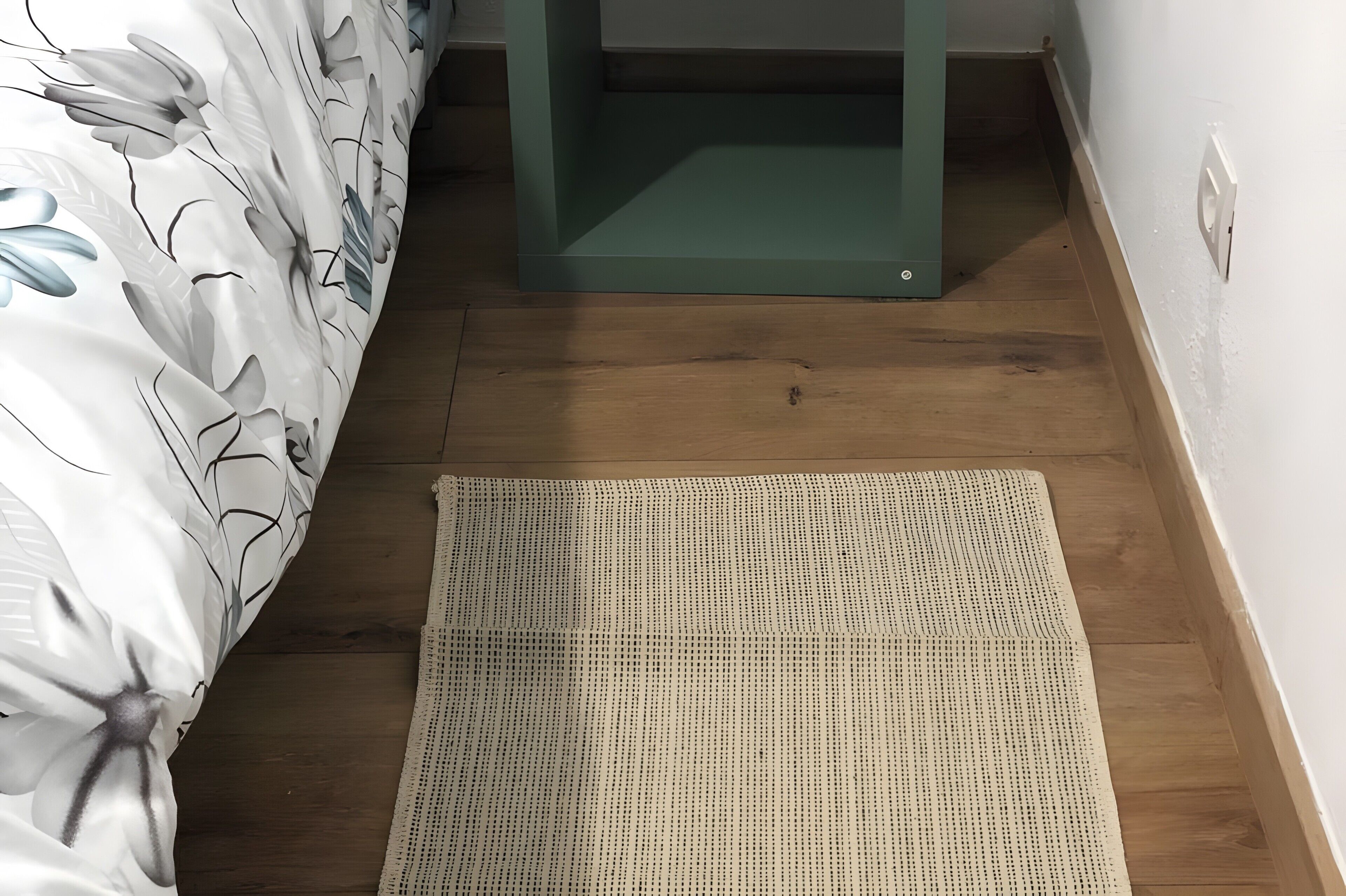 Een slaapkamer met een bed, een nachtkastje in het groen, een geweven vloerkleed en houten vloeren.