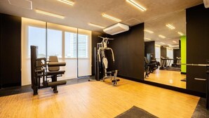 Un gimnasio con equipo de ejercicio, ventanas amplias y un muro de espejos.