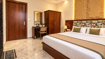 A hotel room with a bed, a desk, a chair, a wardrobe, and a large mirror.