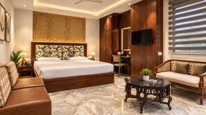 A hotel room with a large bed, a sofa, a desk, and a television. - Hotel Destin (Gwalior)