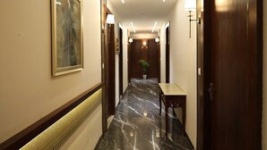 A hotel hallway with marble flooring, wooden doors, and a framed picture on the wall. - Hotel Destin (Gwalior)