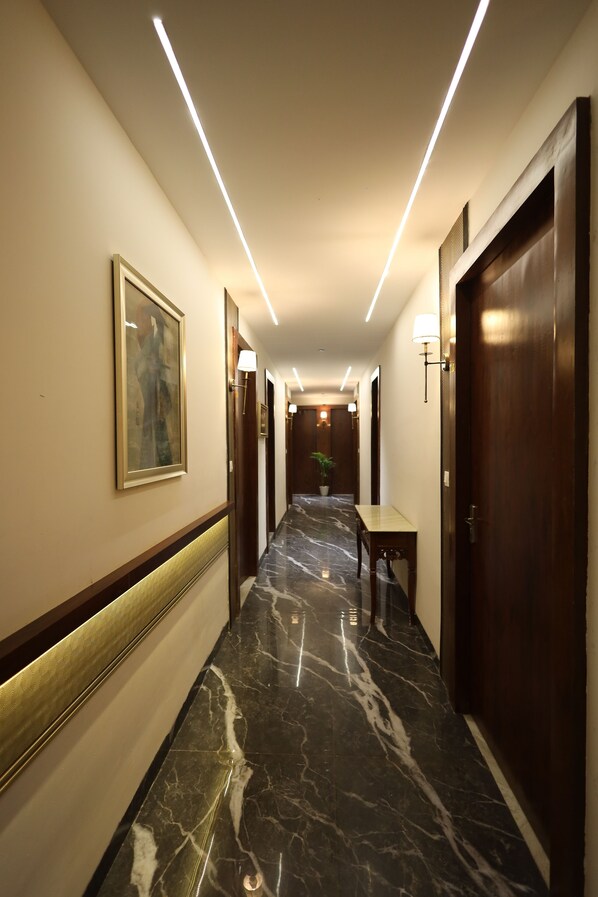 Een hotelgang met marmeren vloeren, houten deuren en een lijst met een afbeelding aan de muur.