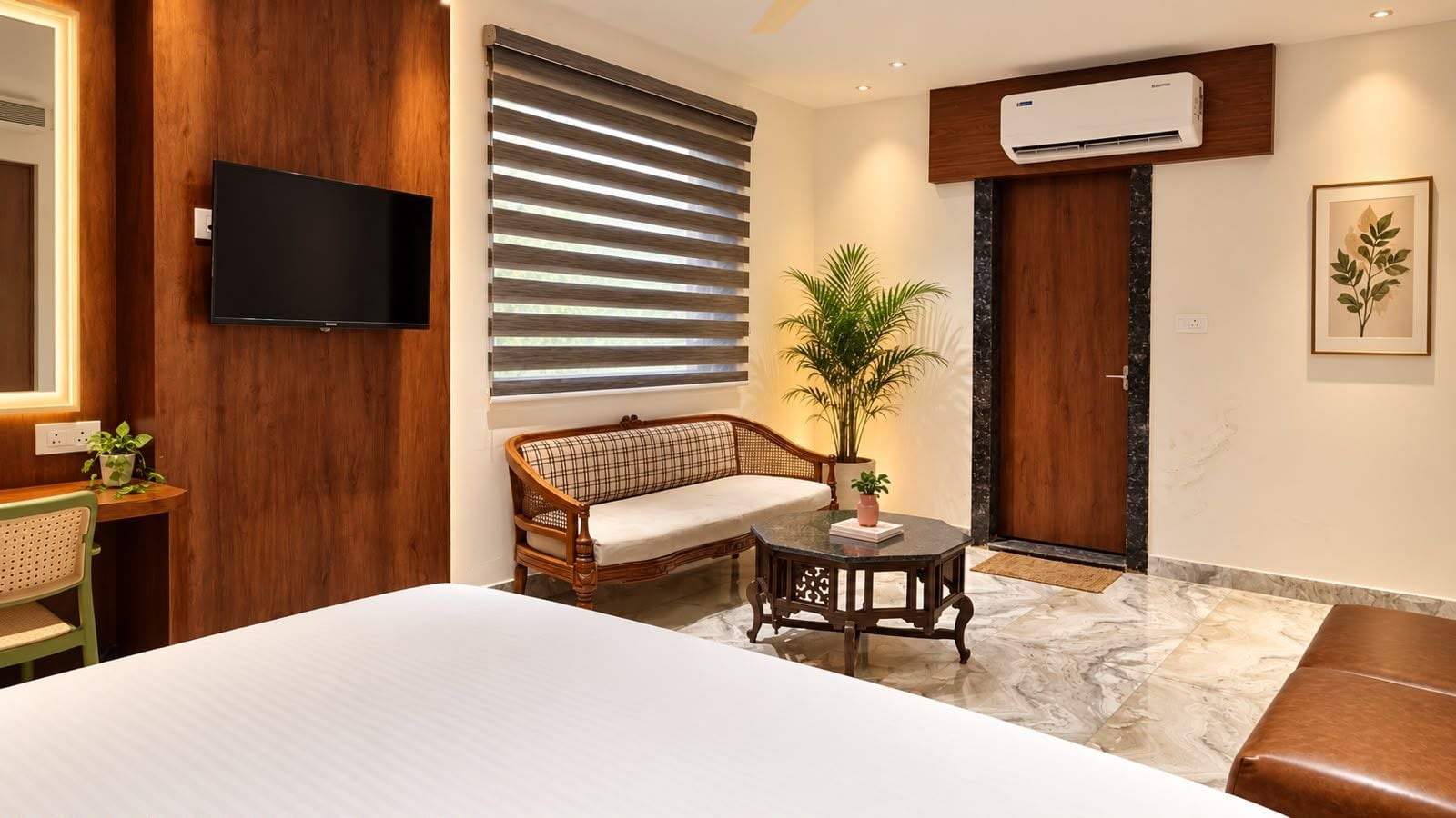 A hotel room with a bed, a television, a sofa, a small table, and a potted plant.