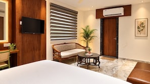A hotel room with a bed, a television, a sofa, a small table, and a potted plant. - Hotel Destin (Gwalior)