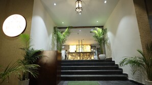 A hotel entrance with a reception desk, a staircase leading to the upper floor, and potted plants. - Hotel Destin (Gwalior)