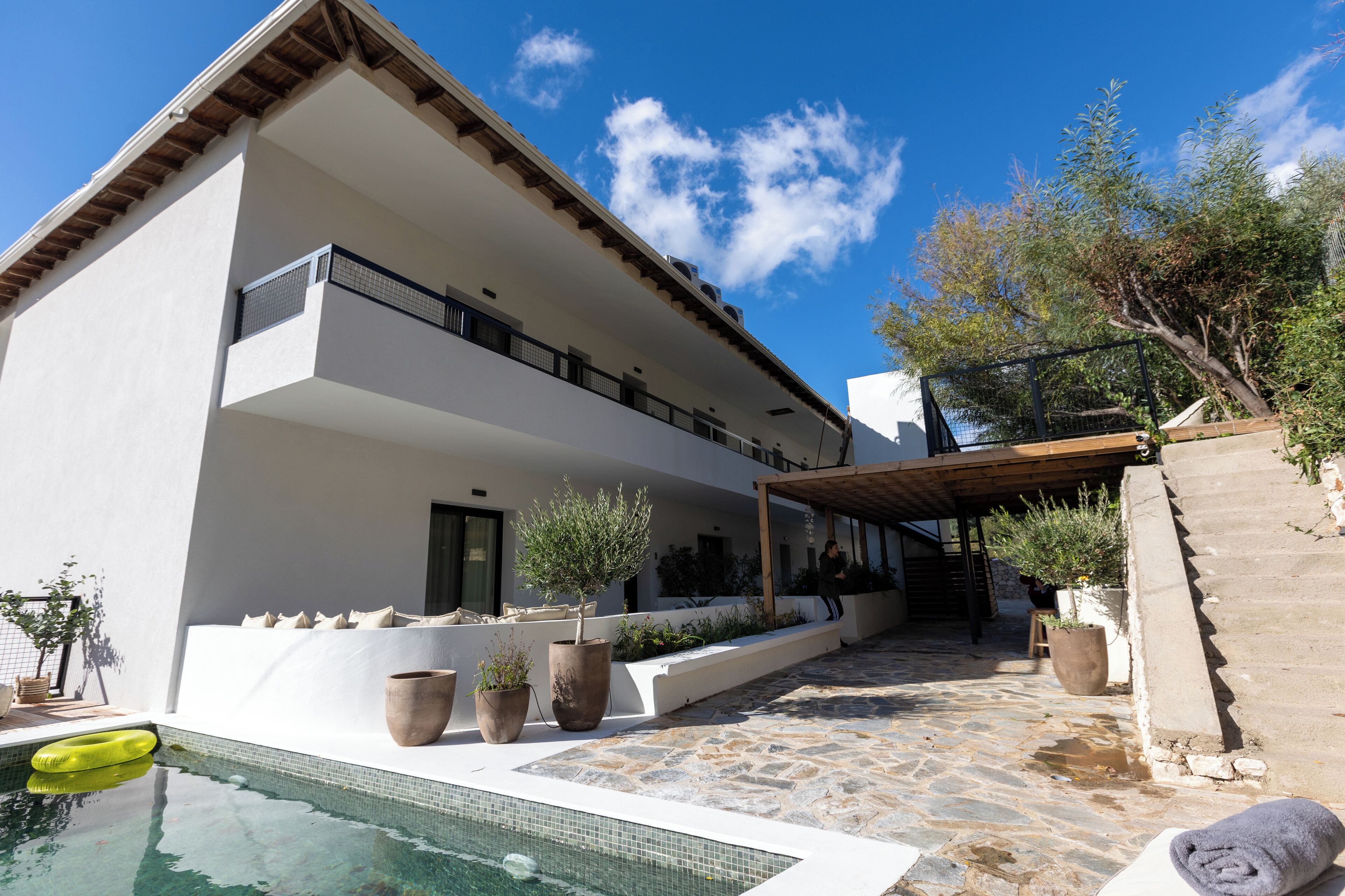 A modern two-story building with a pool, outdoor seating, and potted plants.