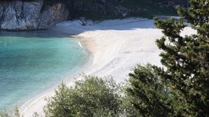 A beach with clear turquoise water and white sand, surrounded by rocky cliffs and greenery.