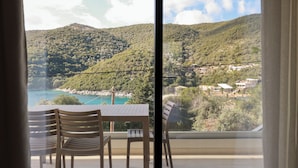 A balcony with a table and chairs overlooking a coastal landscape with hills and a turquoise sea.