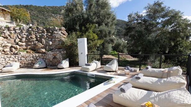 A pool area with a stone wall, lounge chairs, and a wooden deck.