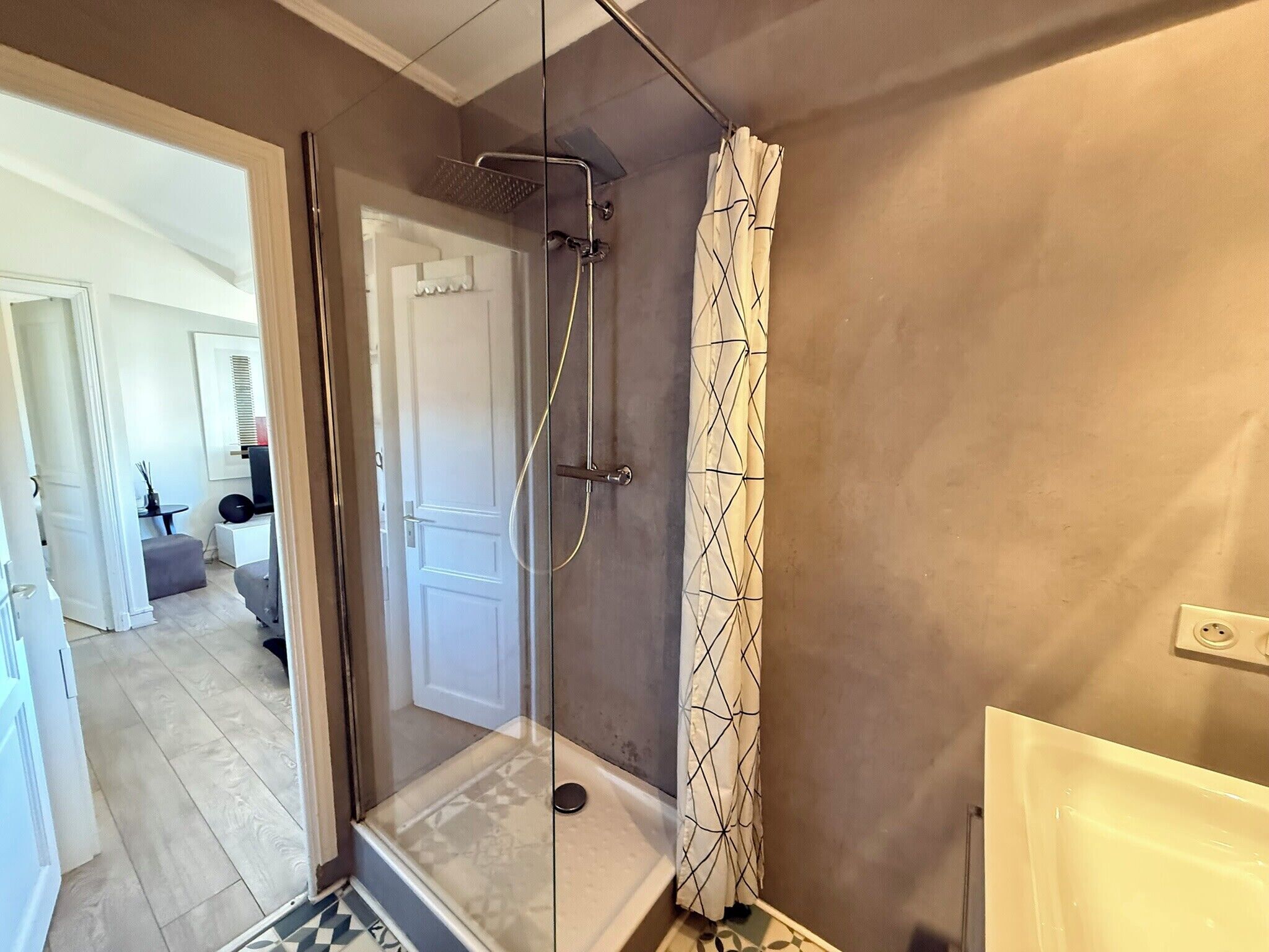 A modern bathroom with a glass-enclosed shower, a patterned shower curtain, and a visible toilet.