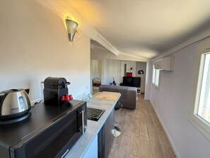 A modern kitchen with a built-in espresso machine, a toaster, and a kettle. There is a dining area with a sofa and a TV. - Nice one-bedroom apartment near the Palais des Festivals (Cannes)