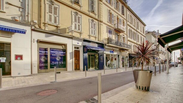 Una strada con edifici, un grande fioriere in metallo con un albero e un tendone blu sopra un negozio.