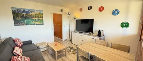 A compact living space with a sofa, a dining table, a TV, and a kitchen area.