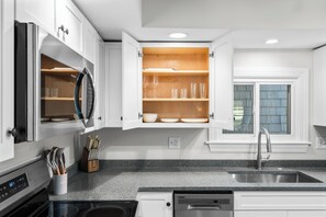 A modern kitchen with white cabinets, a granite countertop, a built-in oven, and a stainless steel sink. - The Essex of Gloucester (Gloucester)