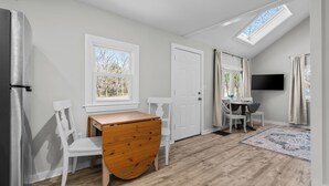 A modern kitchen with white cabinetry, a wooden dining table, and a built-in TV. - The Essex of Gloucester (Gloucester)