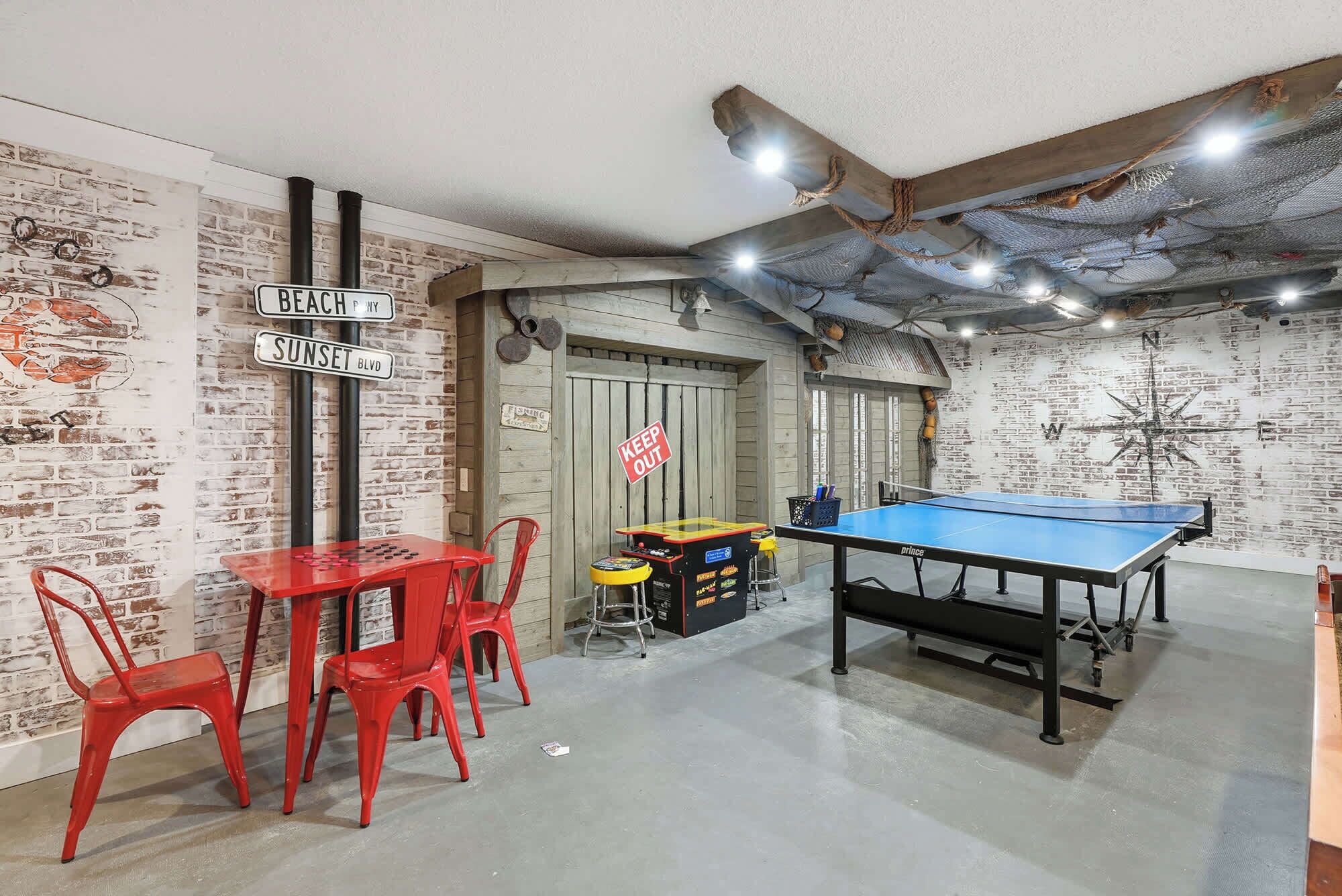 A room with a ping pong table, red chairs, a table tennis table, and a brick wall with street signs.