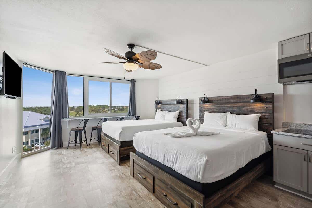 A modern bedroom with two beds, a ceiling fan, and a large window offering a view of the outdoors.