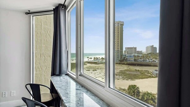Una habitación con un amplio ventanal que da a una playa y al paisaje urbano.