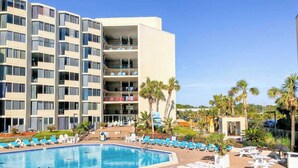 Un hotel con una piscina grande rodeada de tumbonas y palmeras.
