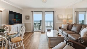 Un soggiorno con TV a schermo piatto, ventilatore a soffitto, balcone con vista e zona pranzo con sedie e tavolo.