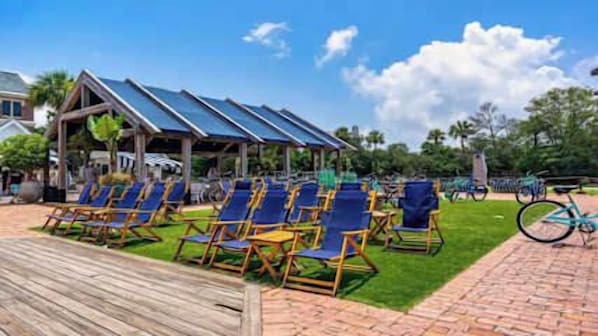 A beachside area with sun loungers, a wooden deck, and a covered seating area with solar panels. - Village of SoWal B203 (Seacrest)