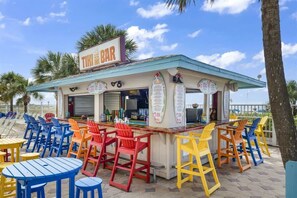 Eine Tiki-Bar mit bunten Stühlen und Tischen, einer Speisekarte und blauem Himmel.