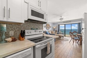 Eine moderne Küche mit weißen Schränken, einem eingebauten Ofen und einer Mikrowelle. Es gibt einen Essbereich mit Tisch und Stühlen sowie einen Blick aufs Meer durch große Fenster.