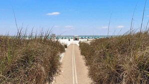 Un sentiero sulla spiaggia conduce a una zona attrezzata con ombrelloni e un gazebo.
