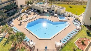 Area piscina di un hotel con una grande vasca centrale, lettini e vista sulla spiaggia.