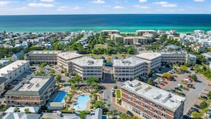 An aerial view of a coastal resort area with multiple buildings, a swimming pool, and a clear view of the ocean. - Village of SoWal B257 (Seacrest)