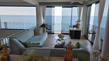 Amplia sala de estar con balcón con vista al mar, amoblada con un sofá, una mesa de centro y objetos decorativos.