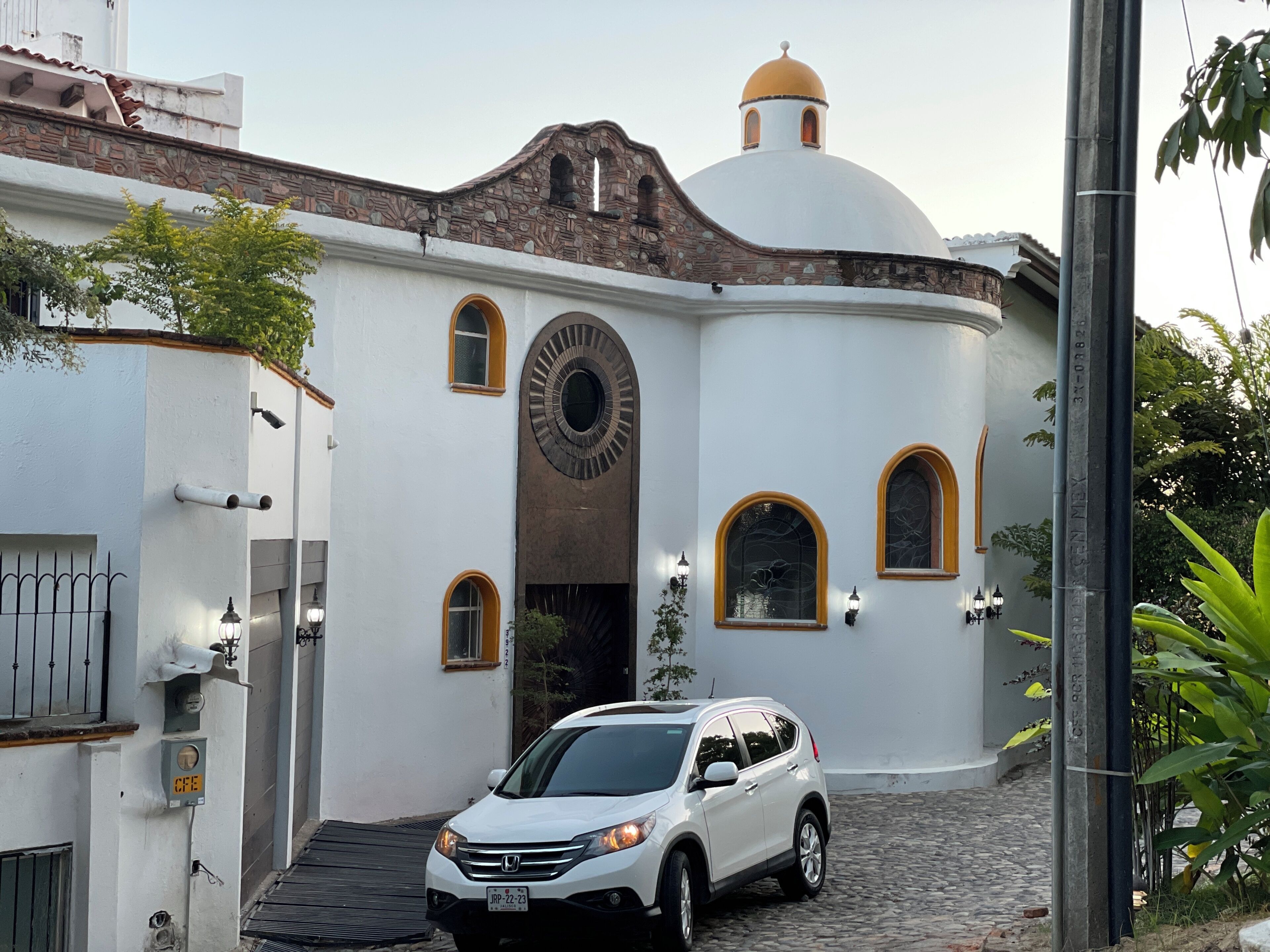 Un edificio blanco con una cúpula y ventanas de arco, un coche blanco estacionado y un camino adoquinado.