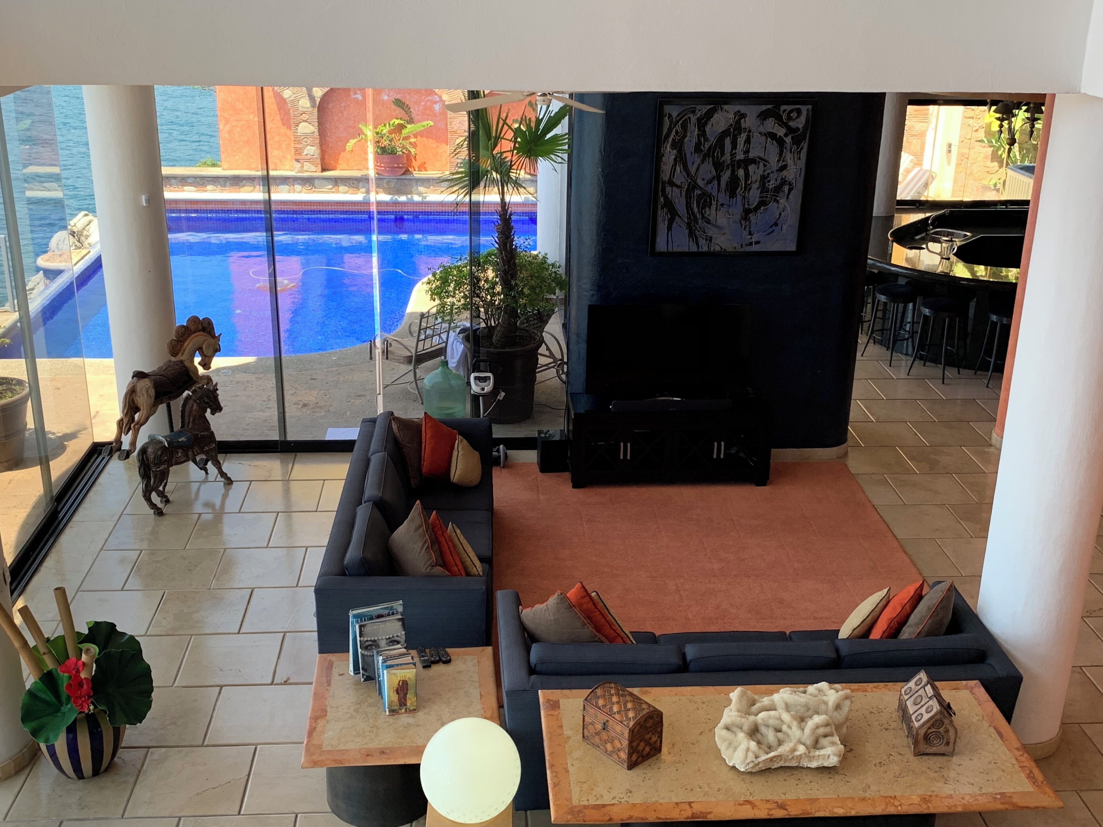 Sala de estar con sofá, mesa de centro y mueble para la televisión. Se ve una piscina a través de puertas de vidrio.