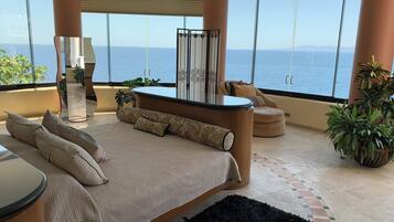 Een slaapkamer met een groot bed, een zithoek en uitzicht op zee.