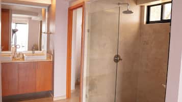 Un baño moderno con ducha de vidrio, tocador con espejo y lavamanos.