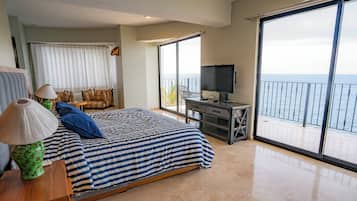 Un dormitorio con cama, escritorio, televisión y balcón con vistas al mar.