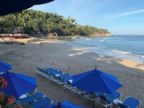 Una playa con sillas de playa y sombrillas, una orilla arenosa y barcos en el agua.