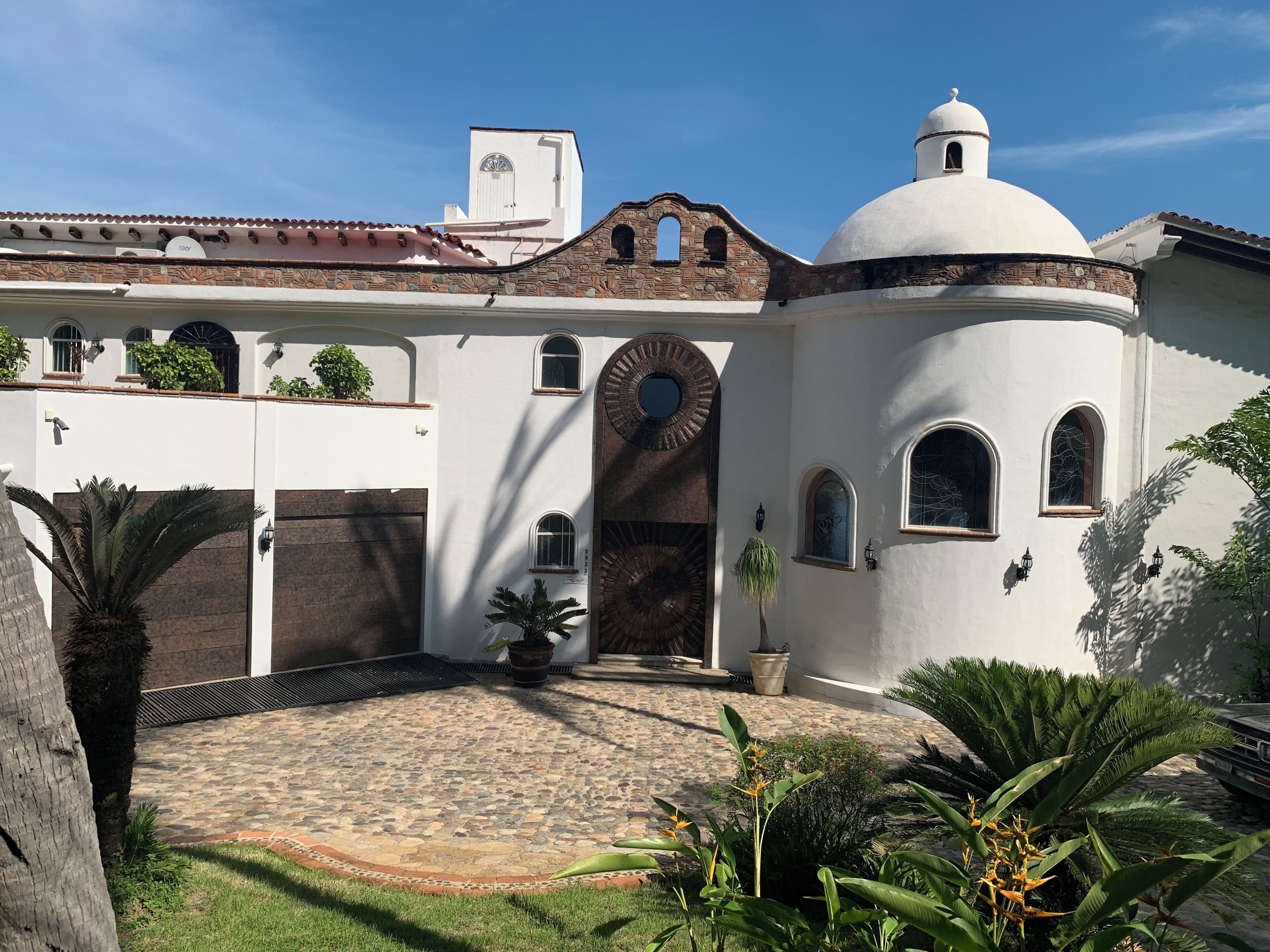 Un edificio con fachada blanca, una cúpula y un patio con suelo de piedra y palmeras.