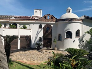 Un edificio con fachada blanca, una cúpula y un patio con suelo de piedra y palmeras.