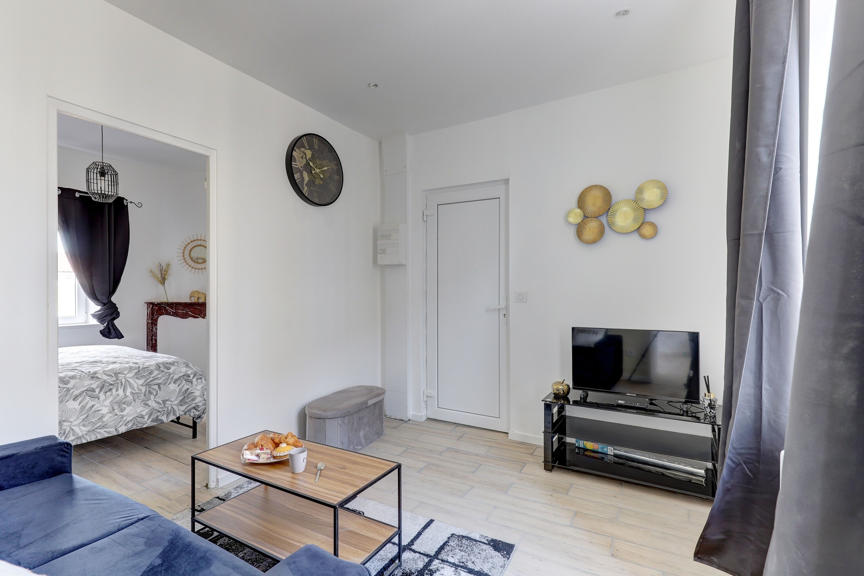 A modern living room with a sofa, a coffee table, a TV, and a bed with a patterned bedspread.