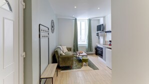A compact living space with a sofa, a small table, a television, and a kitchenette. - Le Cosy Vert - Proche du Cher (Montlucon)