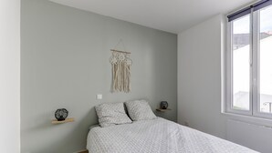 A bedroom with a bed, a macrame wall hanging, and a window with a view of the outside. - Le Cosy Vert - Proche du Cher (Montlucon)
