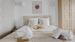 Cama bem arrumada com roupa de cama branca, bandeja com itens de café da manhã e uma obra de arte emoldurada acima.