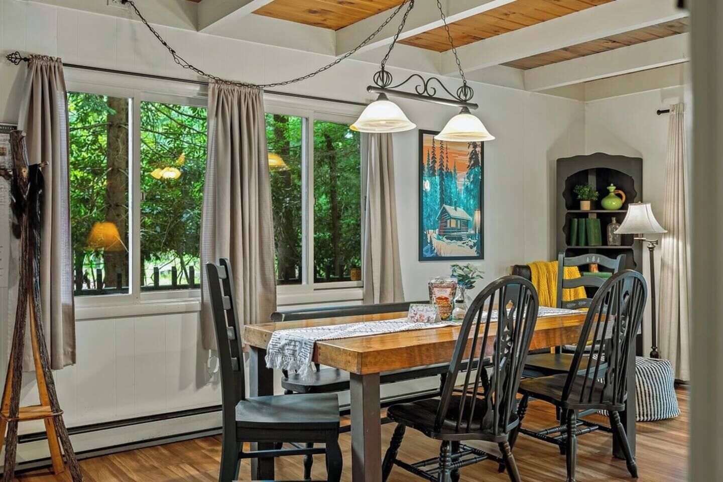 A dining area with a wooden table, four chairs, a painting, and a bookshelf.