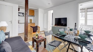 Un salon moderne comprenant un canapé, une table à manger pour quatre personnes, un téléviseur et un coin cuisine équipé d’un four à micro-ondes et de placards.
