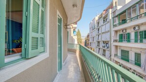 Uma varanda estreita com grades verdes, soalho em azulejos e vista para edifícios vizinhos.
