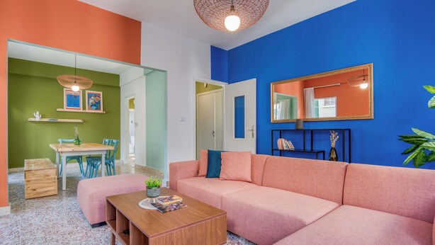 Uma sala de estar com um sofá rosa, uma mesa de centro de madeira e uma parede verde.