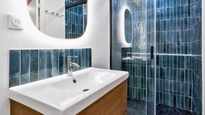 Une salle de bain moderne avec un lavabo blanc, un miroir et une douche dont les murs sont recouverts de carreaux bleus.
