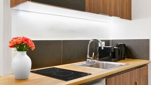 Une cuisine moderne dotée d’un plan de travail en bois, d’une plaque de cuisson à induction noire, d’un évier en acier inoxydable et d’un vase blanc orné de fleurs.
